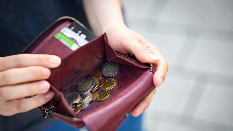 Eine Hand öffnet ein rotes Portemonnaie mit Geldmünzen